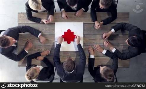 Business people putting the last piece of puzzle on a wooden table, teamwork and problem solution concept, clapping hands