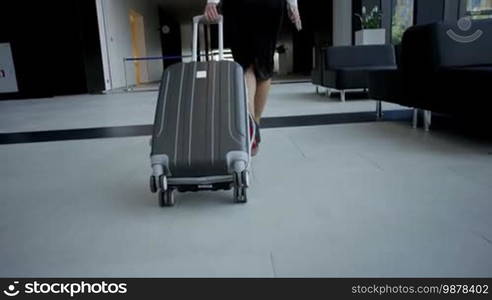 Business woman in formal clothes walking with a wheeled bag at airport terminal