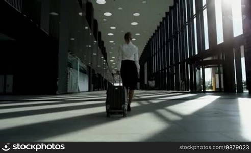 Business woman in formal clothing walking with wheeled bag at airport terminal