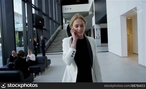 Business woman talking on the phone while walking by the window