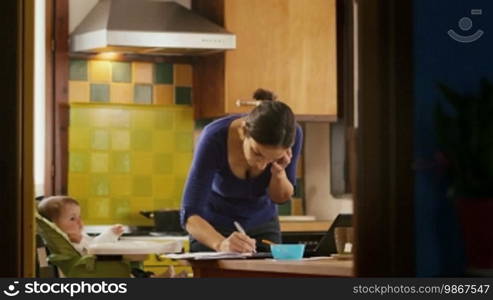 Busy businesswoman with telephone, multitasking mother cooking and working, feeding baby girl at home