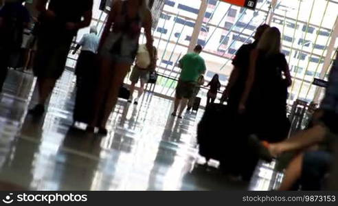 Canted shot of people with luggage, walking down the check-in hall of an airport.