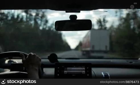 Car overtaking truck on motorway in the forest. View from inside of vehicle's interior. Woman driving car on high-speed motorway and overtaking lorry during summer road trip.