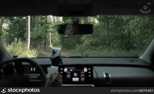 Careful female driver driving car on rural ground road through the forest, searching the place for camping near river during summer vacation. View from inside of vehicle. Driving auto off-road