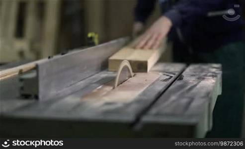 Carpenter working on electric circular saw cutting boards. Closeup of worker's hands cutting wood with table saw in workshop. Skilled carpenter working with industrial tool in wood factory, circular blade with wood board.