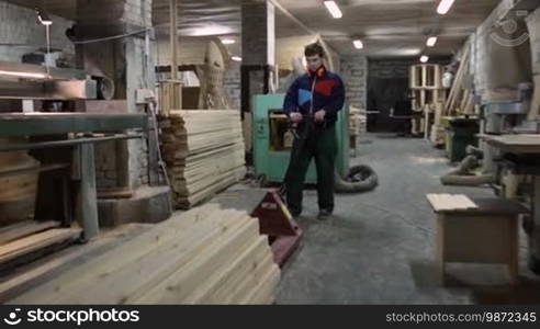 Carpenter working on manual forklift pallet stacked with wooden boards in workshop. Joiner pushing fork pallet truck with stack of planed planks at carpentry shop.