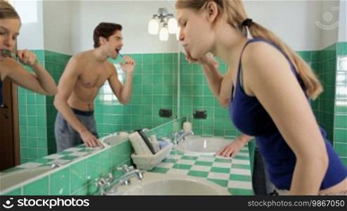 Caucasian heterosexual couple brushing teeth together in bathroom and looking at mirror