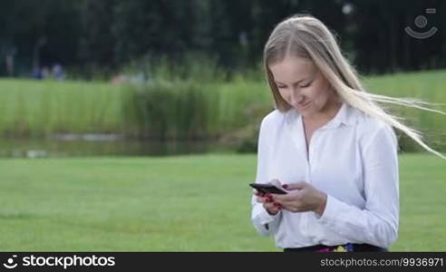 Charming businesswoman working with cellphone outside in the park during freetime. Smiling woman freelancing using a mobile phone outdoor