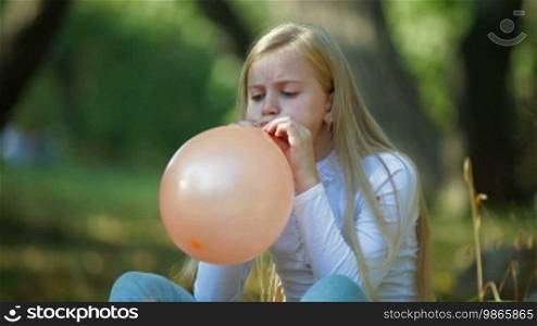 Child Blowing Up a Balloon Outdoors
