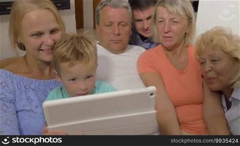 Child, parents, and grandparents looking at a tablet computer. They are watching something interesting on the screen