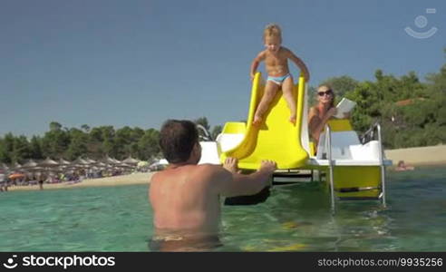 Child riding a slider on pedal boat, father catching him and helping to get back, mother watching them from boat. Family fun on summer vacation