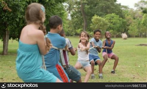 Children and recreation, group of happy multiethnic school kids playing tug-of-war in city park with teacher. Summer camp fun