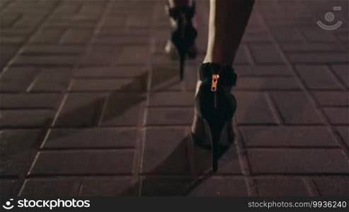 Close up elegant woman's legs on high heel shoes walking away on city street at night. Background night city lights