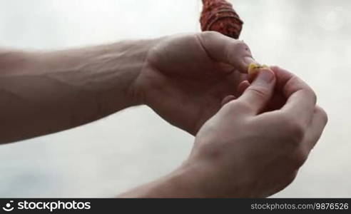 Close up male hands putting corn bait on the fishing hook. Fisherman's hands baiting the hook. The bait for carp. Slow motion.