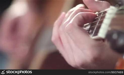 Close up male musician hand playing acoustic guitar with his fingers on frets. Focus on the left hand with shallow depth of field. Guitarist picking chord on classic guitar.