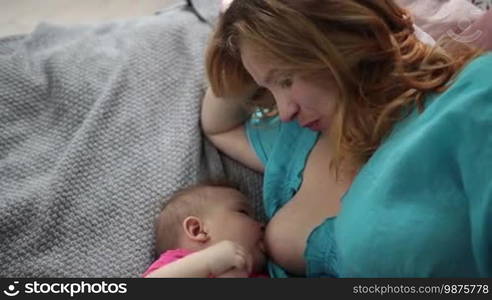 Close-up mother breastfeeding her adorable newborn child while lying on bed. Caring young mom feeding breast to her baby girl at home. Top angle view. Slow motion. Stedicam stabilized shot.