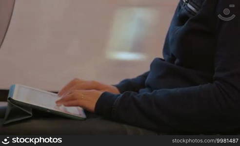 Close-up of a woman sitting by window in the train, holding touch pad on the lap and typing message. Easy communication on the way