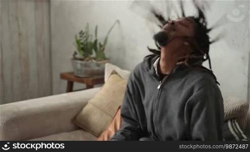 Close up of young African American man with dreadlocks putting on VR headset while sitting on the sofa in domestic interior. Excited man playing video games in virtual reality goggles. Slow motion.