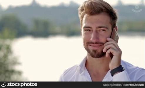 Close up of young handsome hipster talking on the cellphone with his girlfriend over beautiful cityscape background