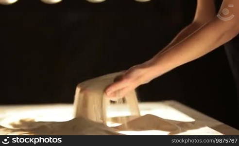 Close-up sand spilling out of female hands against black background in dimmed lights. Artist drawing on the sand, creating sand painting. Hands of a female master creating artwork making sand animation.