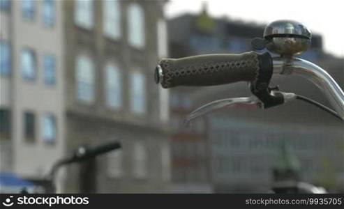 Close-up shot of a handlebar of a bicycle on a defocused background of a city and pedestrians. Traveling on the streets by bike