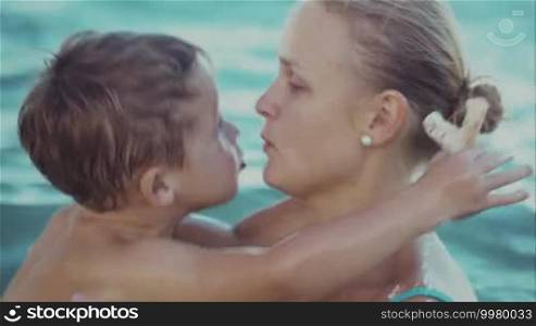 Close-up shot of a little boy kissing beloved mother while they bathe together in the sea