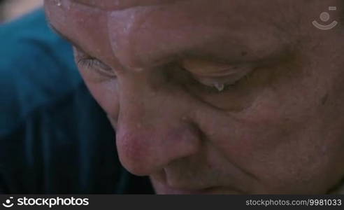 Close-up shot of a mature man being tired and exhausted after intensive training. Beads of sweat rolling on his face