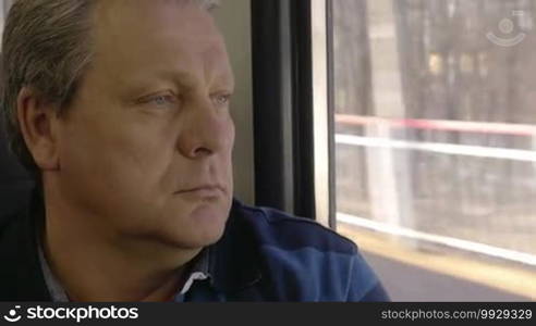 Close-up shot of a senior man having a peaceful time during his travel ride. He is staring through the window with a thoughtful look