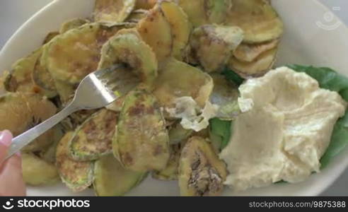 Close-up shot of a woman having a meal with fried zucchini slices and cream sauce