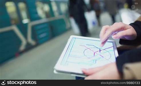 Close-up shot of a woman looking at a metro map on a pad while she waits at an underground station