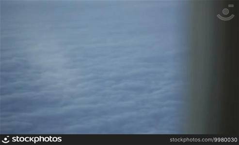 Close-up shot of a woman looking out the window in a plane, with solid clouds beneath. Initially focusing on the clouds, then on the woman