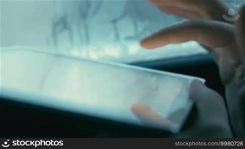Close-up shot of a woman's hand typing email or chat message on a tablet computer while traveling by car