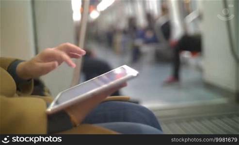 Close-up shot of a woman typing on a tablet PC while traveling by underground train