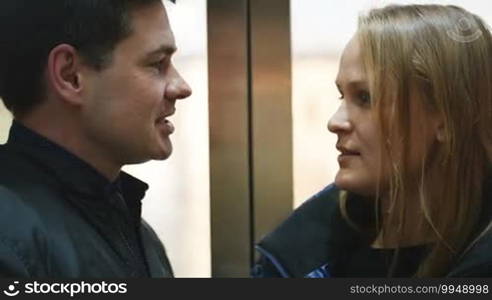 Close-up shot of a young man and woman having a talk while going down in an elevator