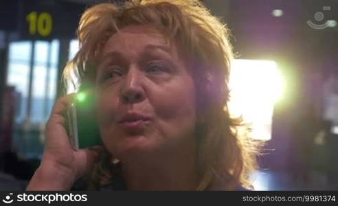 Close-up shot of cheerful senior woman talking on cell phone at the airport terminal