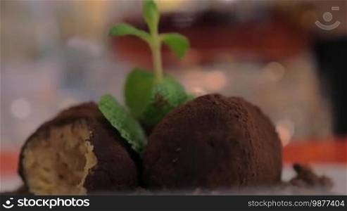 Close-up shot of eating a dessert in the restaurant. Sweet balls with cocoa coating, chocolate soil, and mint