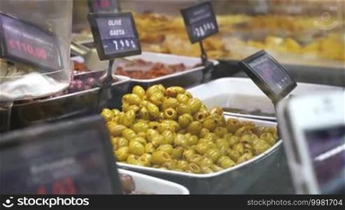 Close-up shot of female hand with smartphone taking a photo of marinated olives presented on shop display