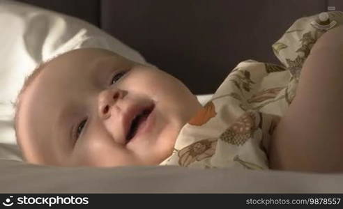 Close-up shot of lovely smiling blue-eyed baby girl of six months old lying on bed at home