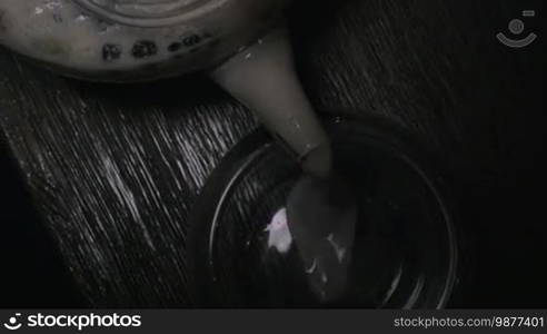 Close-up shot of pouring Indian masala tea from glass teapot into a tea bowl. Top view