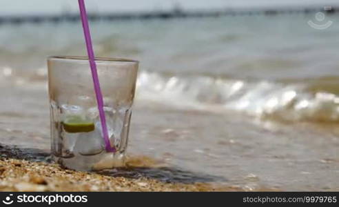 Close-up shot of putting lemon slice and pouring fizzy drink into glass with ice standing on the sand by the sea