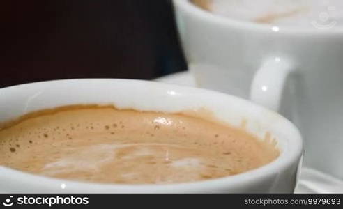 Close-up shot of putting sugar into cup with coffee and stirring it with spoon