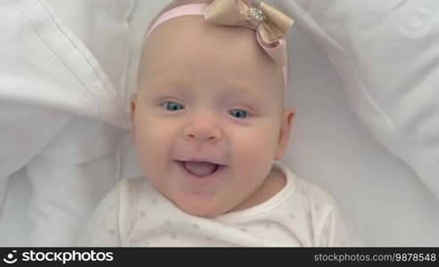 Close-up shot of six-month-old baby girl with a bow. Portrait of a happy blue-eyed child lying on bed