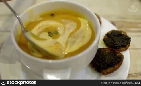 Close-up shot of stirring cream soup with a spoon. Soup served with two bruschettas