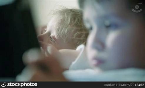 Close-up shot of two brothers with changing focus. One kid watching TV, the other using touchpad