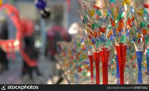 Close-up shot of wine glasses in the store decorated with colorful elements. Beautiful and famous Venetian glass. People walking in the street in the background