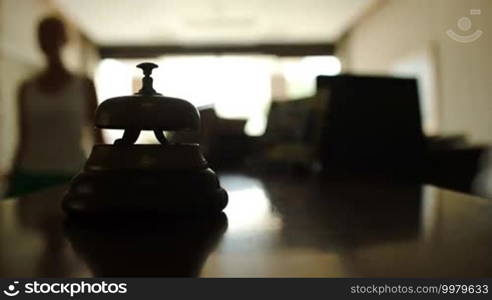 Close-up shot of woman coming up to hotel counter desk and ringing reception bell