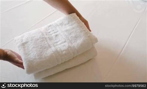 Close-up shot of woman putting two fresh clean towels on the bed with white sheet