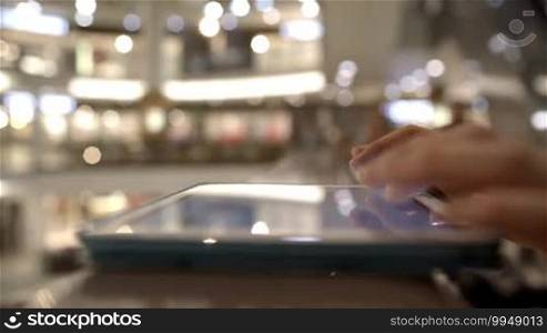 Close-up side shot of woman's hands typing on pad on handrails in shopping center