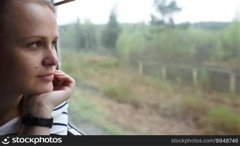 Close-up view of a young woman looking out the window and enjoying passing landscape while traveling by train
