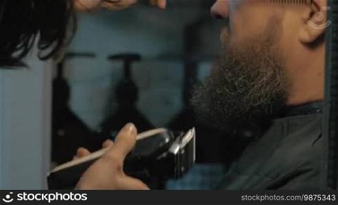 Close up view of female barber taking care of lush beard of white old man. Barber combing and trimming beard